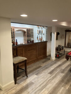 Custom built home wine bar with wooden countertops, glass and wood shelving, and bright modern lighting in Furlong, Pennsylvania