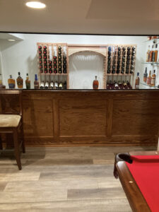 Custom built home wine bar with wooden countertops, glass and wood shelving, and bright modern lighting in Furlong, Pennsylvania