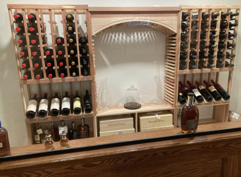 Custom built home wine bar with wooden countertops, glass and wood shelving, and bright modern lighting in Furlong, Pennsylvania